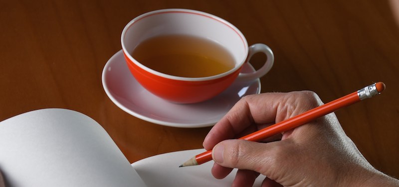 Eine schreibende Hand, daneben eine Tasse Tee.