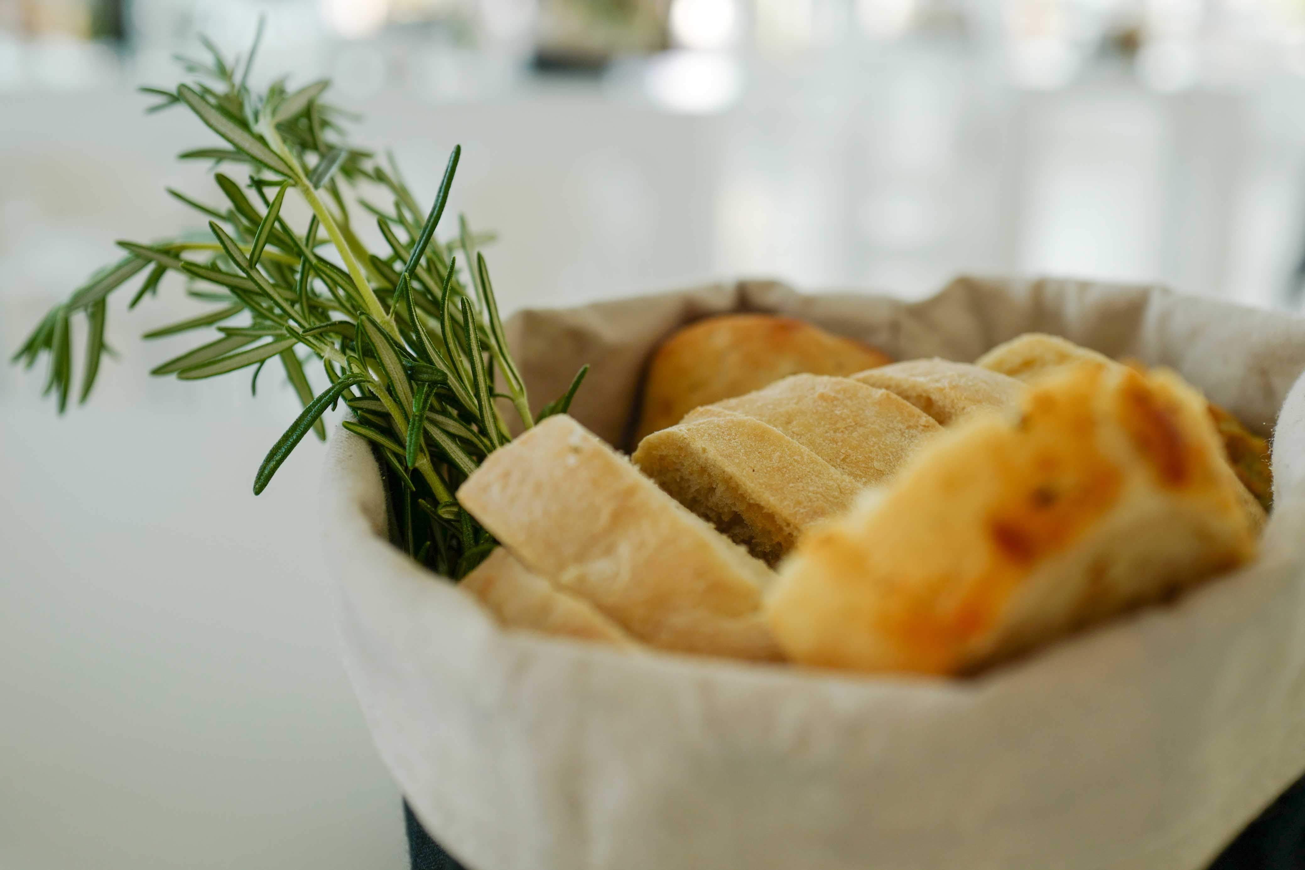 In Nahaufnahme fotografiert ist ein Brotkörbchen mit Baguettestücken und ein Rosmarinstrauß